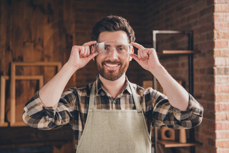 Photo of positive woodworker guy hold touch wear protective goggles for work in garageの写真素材