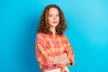 Confident young woman with curly hair standing against a bright blue background, expressing a modern and stylish attitudeの写真素材