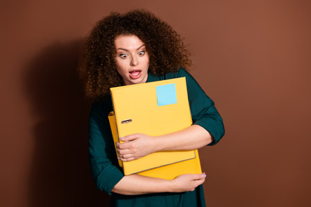 Photo of adorable impressed woman wear formal shirt holding documents folders empty space isolated brown color backgroundの写真素材