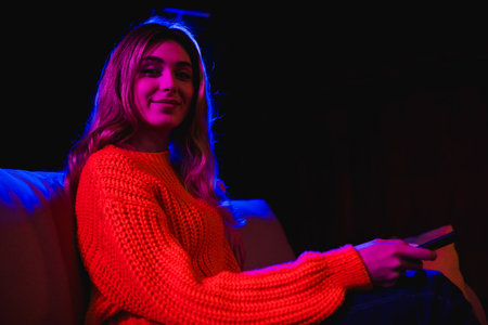 Photo of lovely young girl sit sofa remote controller sit sofa watching tv streaming movie big television screen neon light homeの写真素材