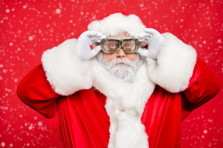 Close up photo of focused funky cool santa claus fix his goggles before rocket flight wear white gloves cap isolated over red color backgroundの写真素材