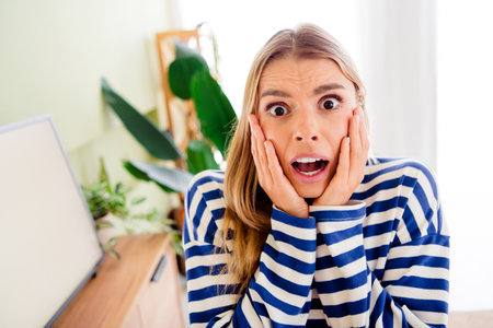 Photo of attractive blonde young woman white screen watch tv frightened dressed striped outfit cozy day light home interior living roomの写真素材