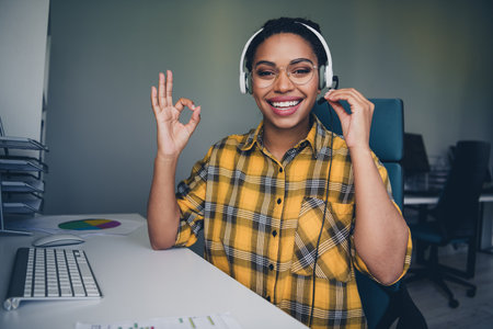 Photo of attractive young woman call center okey symbol wear yellow plaid shirt comfortable modern...