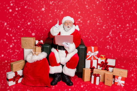 Full body photo of impressed santa claus with eyewear eyeglasses spectacles use device have genius thoughts wearing headwear hat belt isolated over red backgroundの写真素材