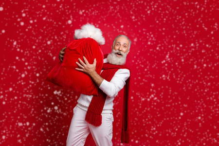 Hipster grey haired man unusual santa with traditionally large bag wear fashion knitted clothes isolated red backgroundの写真素材