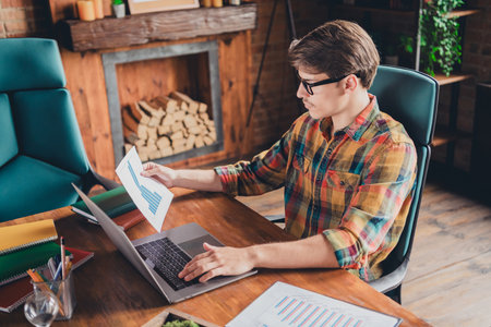 Photo of handsome man wear shirt sit table hold paper analyzing report stats workplace workspace indoors office loft interiorの写真素材