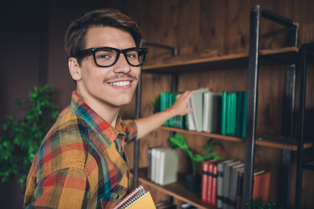 Photo of handsome clever intelligent man wear checkered shirt choose book indoors college university libraryの写真素材