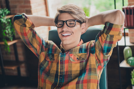 Photo of handsome young man wear checkered shirt sit chair hold arms behind head done finish loft interior indoorsの写真素材