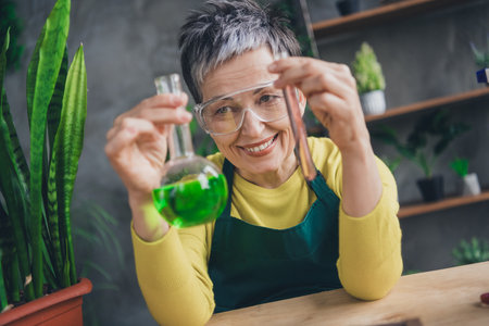 Photo of nice elderly lady creating fertilizer, wearing a green apron, enjoying gardening indoors.の写真素材