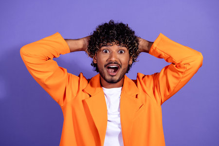 Photo of cheerful impressed guy dressed orange jacket hands arms head emtpy space isolated purple color backgroundの写真素材
