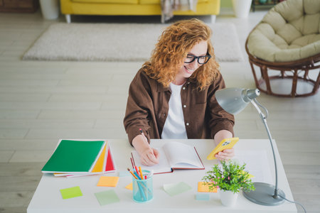 Photo of positive lovely girl wear shirt sit table remote work from home freelance indoors workplace workspaceの写真素材