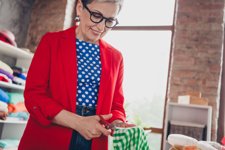 Cropped photo of aged clothing designer lady cut fabric loft interior office studio indoorsの写真素材