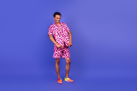 Stylish young man posing in pink leopard print outfit on violet background exudes confidence and glamourの写真素材