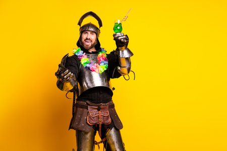 Medieval Knight in Armor Celebrating with a Drink in Front of a Yellow Backdropの写真素材
