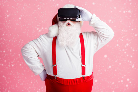 Portrait of attractive impressed bearded Santa watching vr wear helmet enjoying pastime weekend isolated pink pastel color backgroundの写真素材