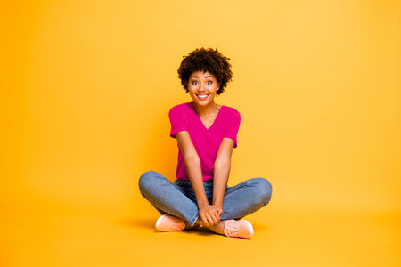 Full length body size photo of curly cheerful funny cute sweet nice pretty african woman sitting on floor with her legs crossed wearing jeans denim isolated voer bright color backgroundの写真素材