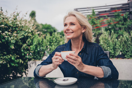 Elderly woman enjoying a relaxing coffee break outdoors in a city garden.の写真素材