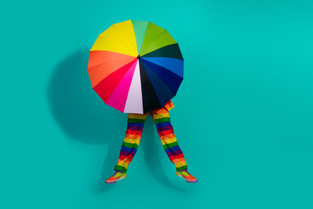 Colorful fashion concept featuring a rainbow-striped outfit and umbrella against teal backgroundの写真素材