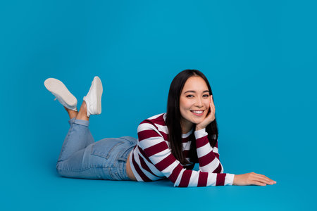 Smiling young woman in casual striped shirt posing on blue backgroundの写真素材