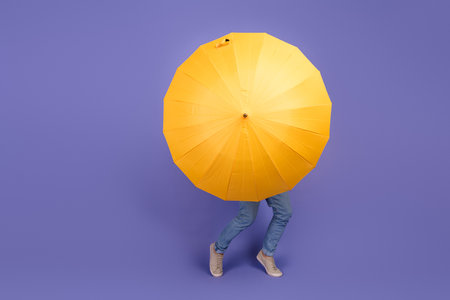 Playful scene featuring a vibrant yellow umbrella with a mid-motion individual behind, creating a joyful and colorful contrastの写真素材