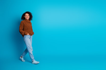 Young woman in a brown knitted sweater against a blue background smiling in a casual trendy fashion poseの写真素材