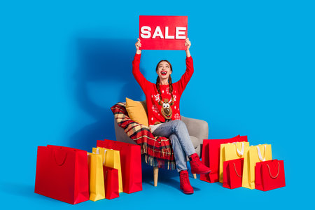 Full body photo of young woman shopping bags raise look up sale plate dressed red christmas clothes theme party on blue color backgroundの写真素材
