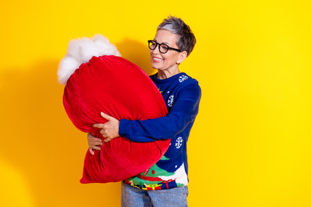 Photo of cute cheerful senior lady wear blue trendy clothes hand hold big red bag isolated on yellow color backgroundの写真素材