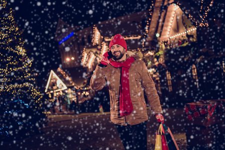 Portrait of peaceful positive guy speak communicate telephone hold shop bags trade buy souvenirs newyear lights outsideの写真素材