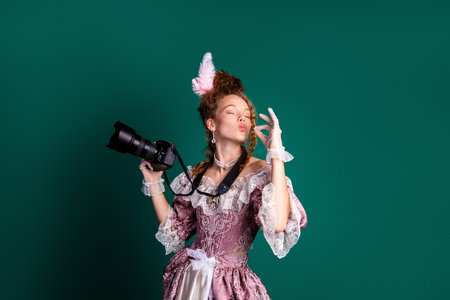 Woman in an Elegant Baroque Costume Holding a Modern Camera Against a Green Backgroundの写真素材