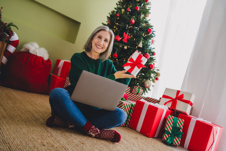 Photo of charming pretty woman sit floor wear green pullover hold present new year preparation atmosphere indoors homeの写真素材