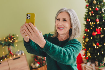 Photo of cute lovely woman dressed green stylish clothes hold phone video call christmas atmosphere indoors homeの写真素材
