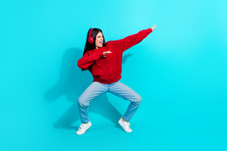 Young woman dancing joyfully in a casual red sweater and jeans wearing headphones on a vibrant backgroundの写真素材