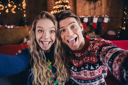 Photo of funky charming couple dressed ornament pullovers tacking selfie stick out enjoying x-mas day indoors house apartment roomの写真素材