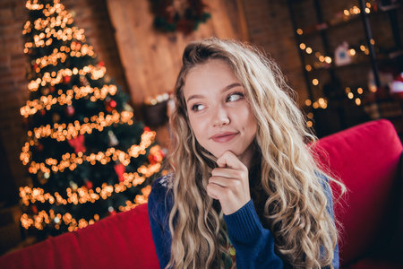 Photo of lovely blonde teenager woman look empty space minded dressed christmas outfit day light home party decoration interior roomの写真素材
