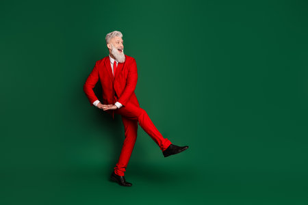 Full size photo of stylish classy santa have fun dance look empty space wear red christmas suit isolated on green color backgroundの写真素材