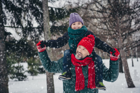 Photo of cute friendly little child dressed in coats having fun together riding on shoulders outdoors in an urban forest parkの写真素材