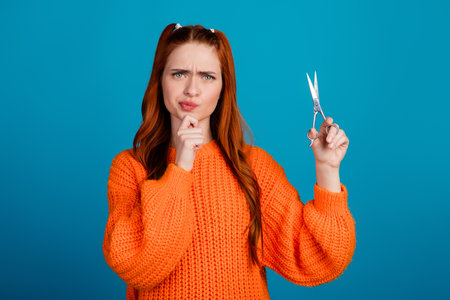 Photo of thoughtful pretty lady dressed in pullover rising scissors empty space isolated blue color backgroundの写真素材
