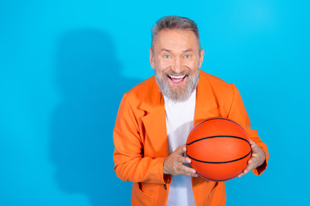 Photo of funny trendy aged man hold basketball empty space wear orange costume isolated on blue color backgroundの写真素材