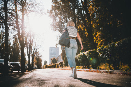 Full body photo of young blonde woman walking back view wear khaki clothes tied shoulders sweater outside urban city parkの写真素材