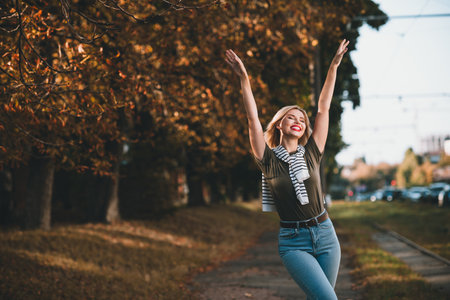 Photo of pretty young blonde woman raise hands posing have fun wear khaki clothes tied shoulders sweater walk outside urban city parkの写真素材