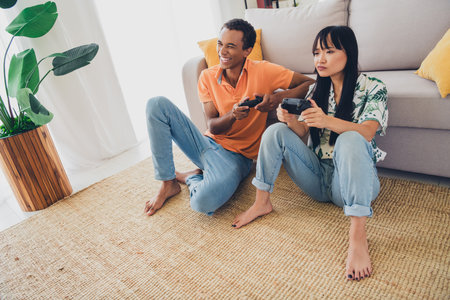 Photo of funny cute couple wear t-shirts enjoy weekend together play playstation indoors living room apartmentの写真素材