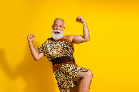 Photo of excited old man enjoy raise fists up wearing animal fur isolated yellow color backgroundの写真素材