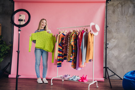 Full length portrait of nice young girl show clothing smart phone holder record blog video...