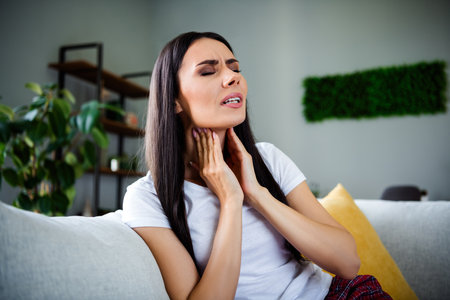 Photo of pretty young lady sit couch touch neck sick throat wear pajama weekend modern interior apartment indoorsの写真素材