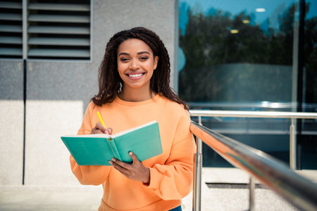 Photo of pretty cheerful lady wear orange jumper writing copybook outdoors urban city streetの写真素材