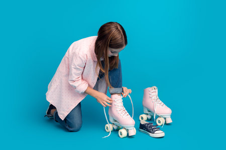 Young girl lacing pink roller skates on a vibrant blue background, showcasing trendy style and casual fashion.の写真素材