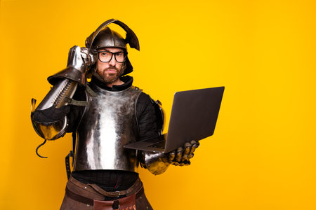 Knight in armor holding a laptop showcasing a blend of modern technology and medieval flair on yellow backgroundの写真素材