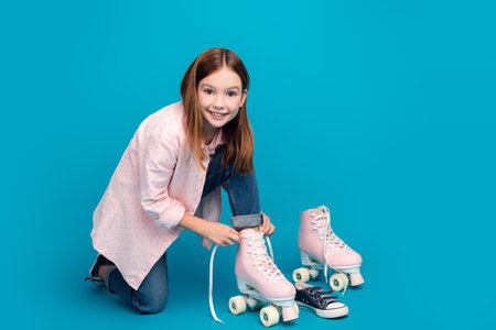 Smiling young girl with roller skates on blue background, dressed in casual stylish outfit, brown hairの写真素材