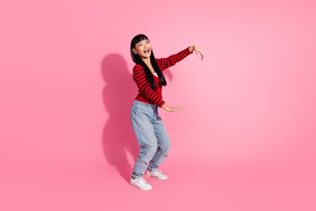 Smiling woman posing playfully in stylish casual wear against pink backgroundの写真素材