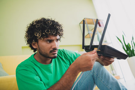 Portrait of nice young man put connect internet cable router wear t-shirt modern green interior flat indoorsの写真素材